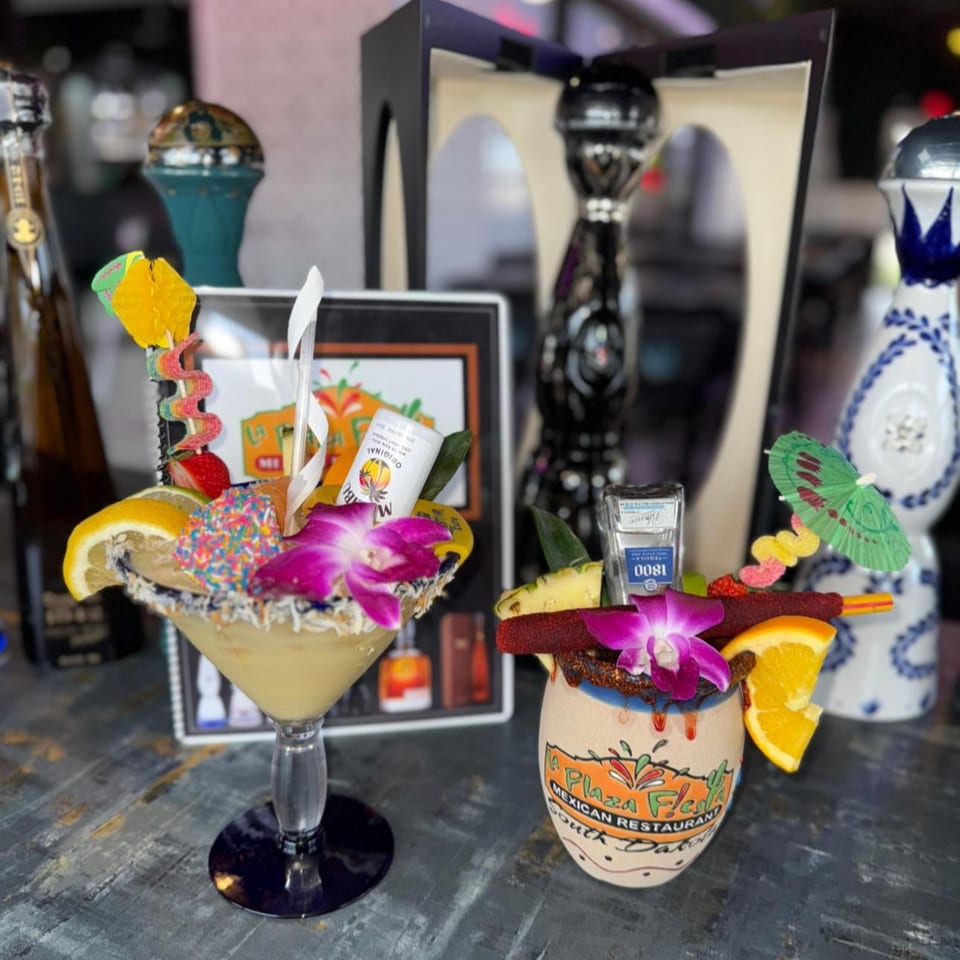 Two elaborately garnished La Plaza Fiesta margaritas, one in a martini glass, the other in a ceramic mug.