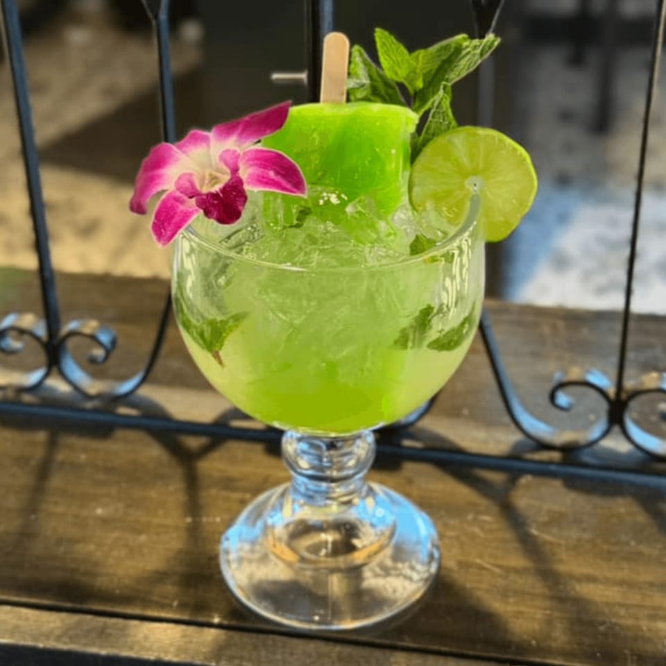 A bright green La Plaza Fiesta margarita with a popsicle, lime, mint, and orchid garnish.