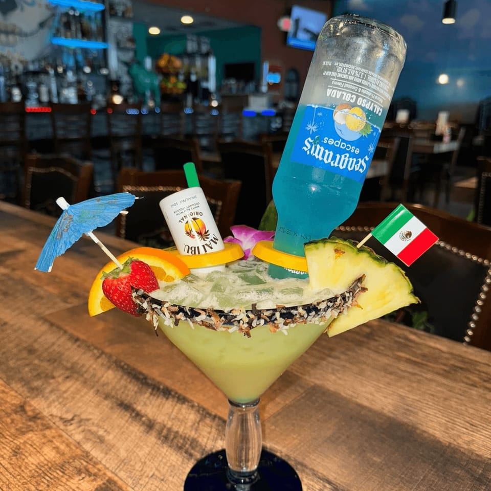 A large green margarita with a Seagram's bottle, Malibu shot, fruit, and Mexican flag.