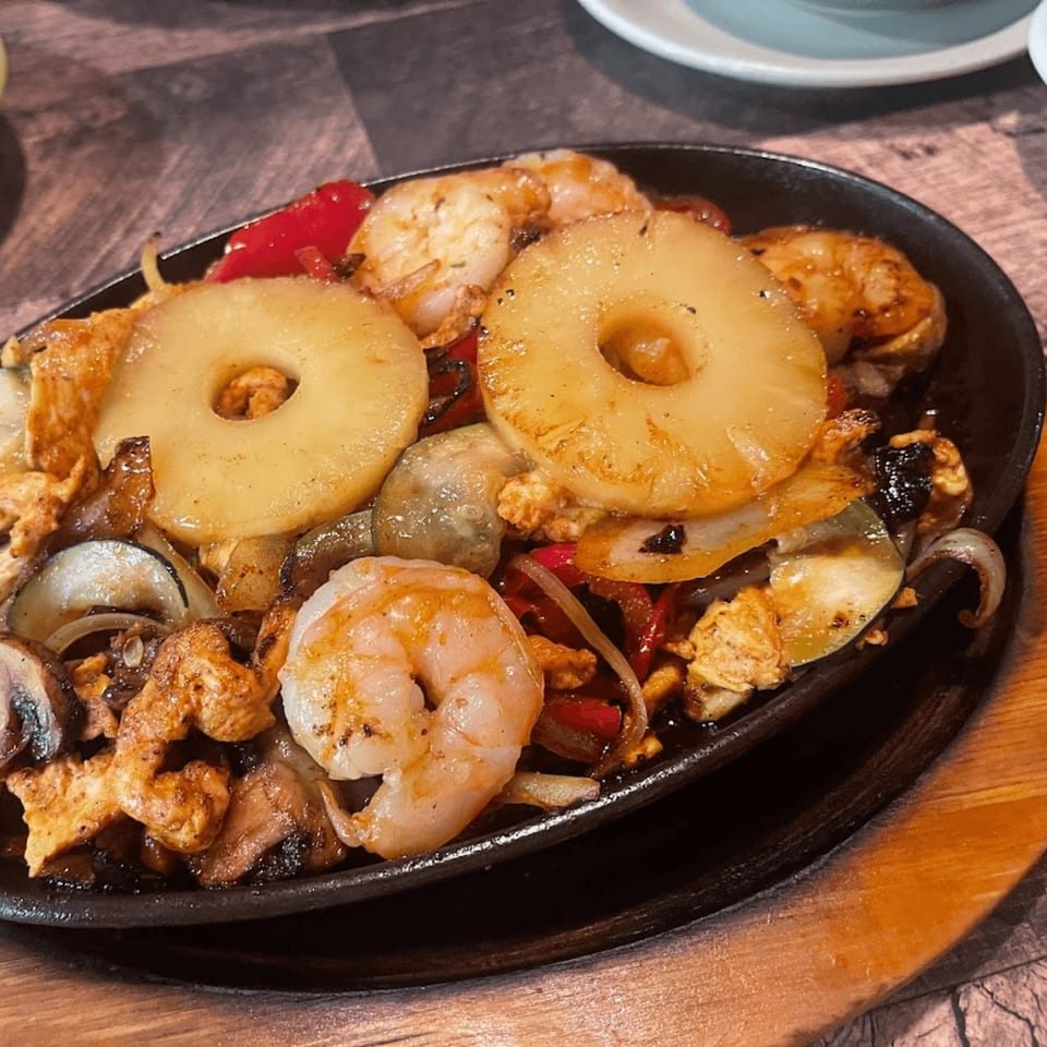 Sizzling fajitas with shrimp, chicken, pineapple, onions, and peppers in a black skillet.
