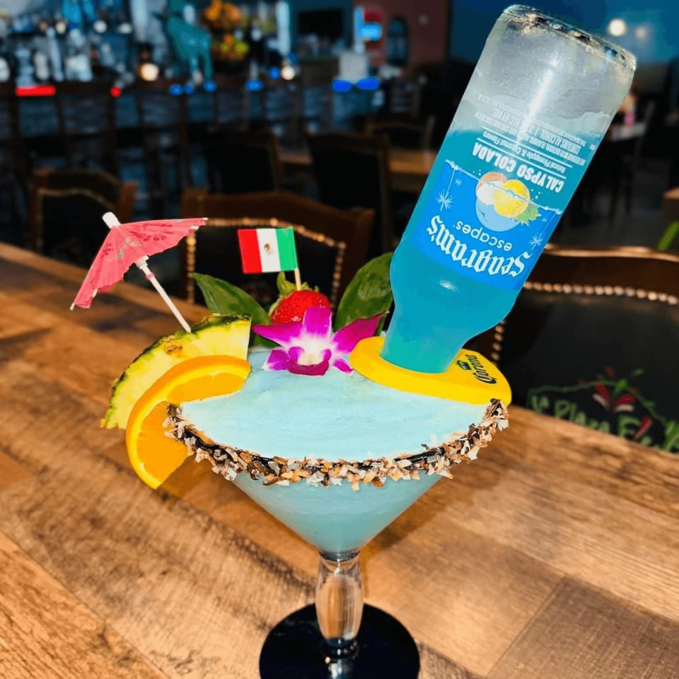 A blue margarita with a Seagram's Calypso Colada bottle inverted into it, garnished with fruit and a Mexican flag.