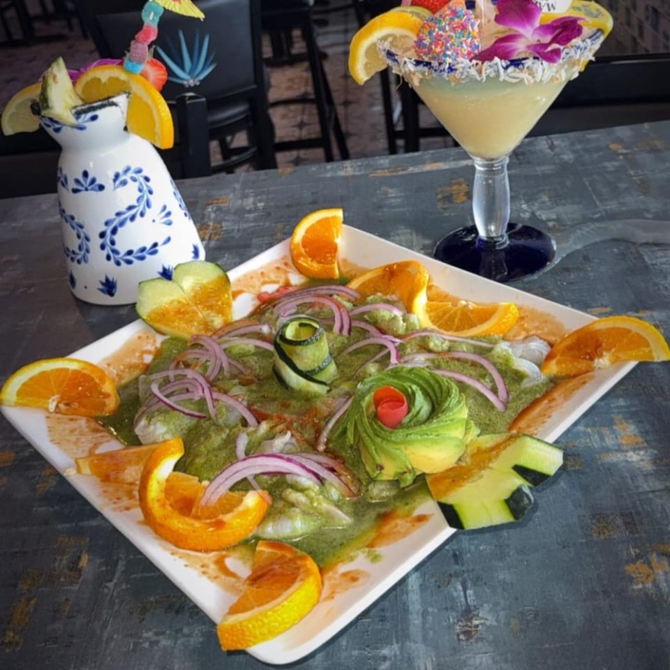 Mexican ceviche with shrimp, avocado, red onion, and oranges, next to a margarita and a decorative pitcher.